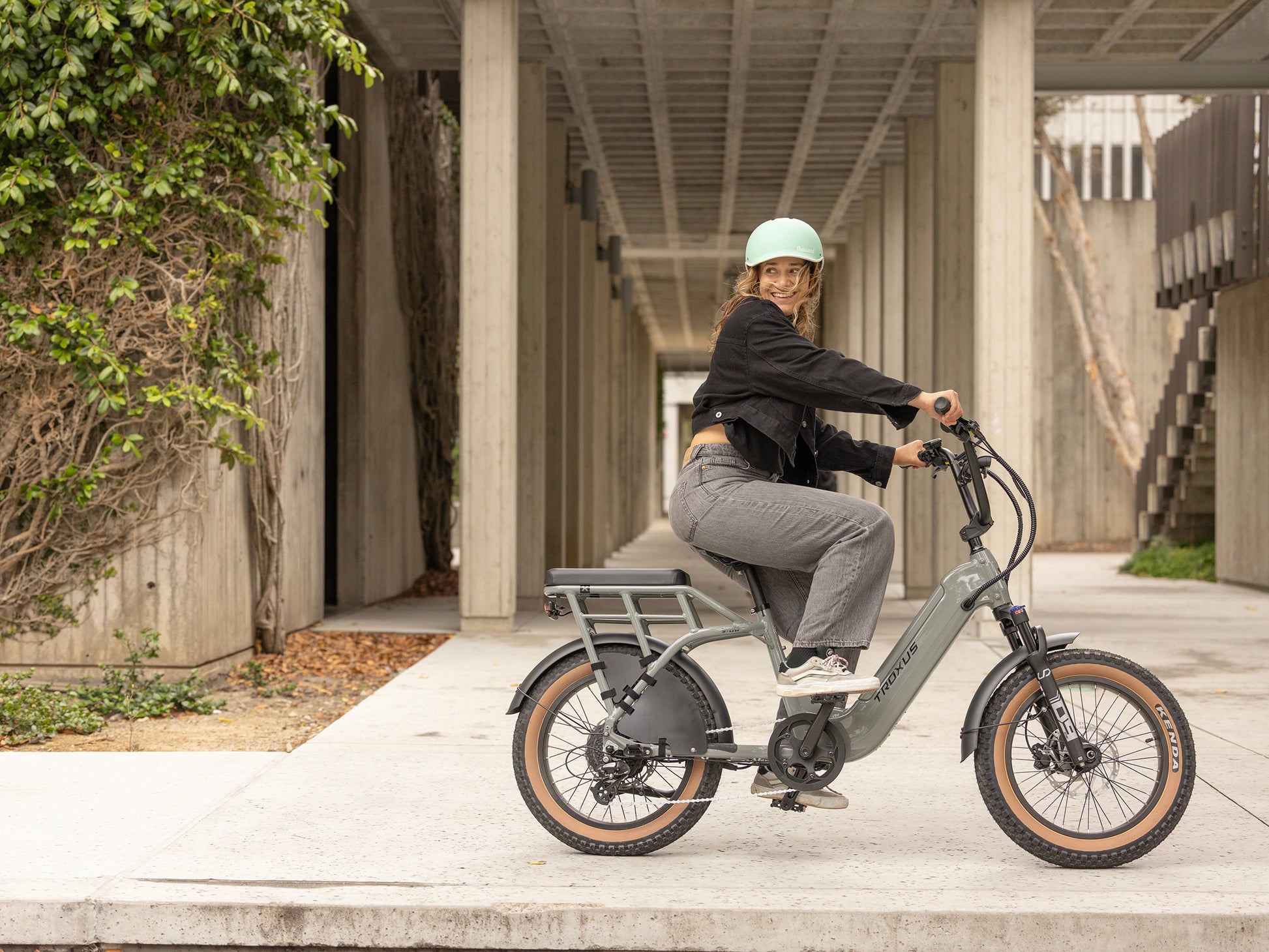 Rider cruising a grey Troxus Lynx 2-Up electric bike with step-thru frame, passenger seat and 20 inch fat tires in an urban setting