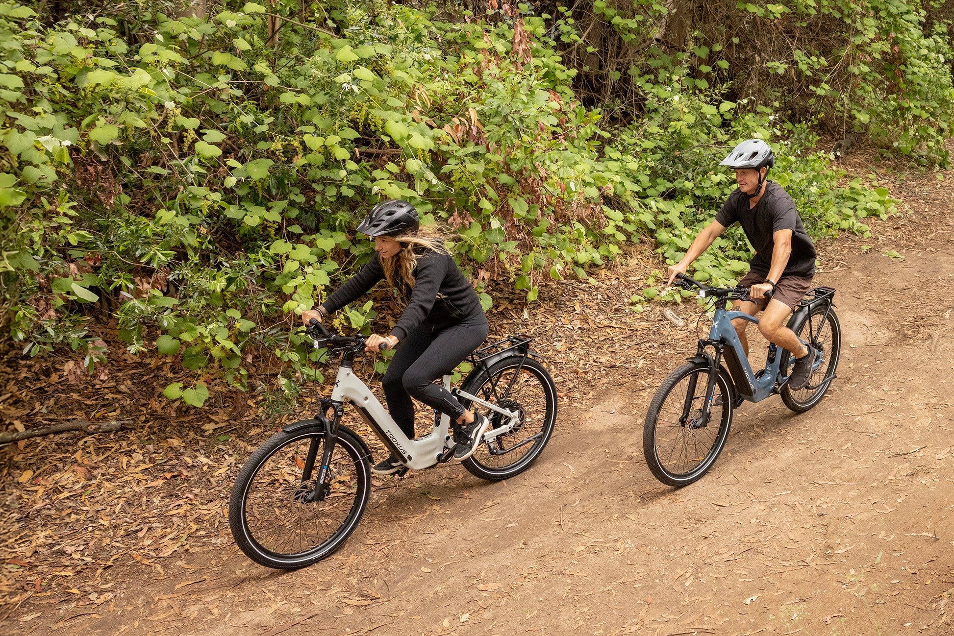 Two riders enjoying a forest trail on Troxus Trax SUV electric bikes in Cadet Blue and Chalk, showcasing comfort and versatility