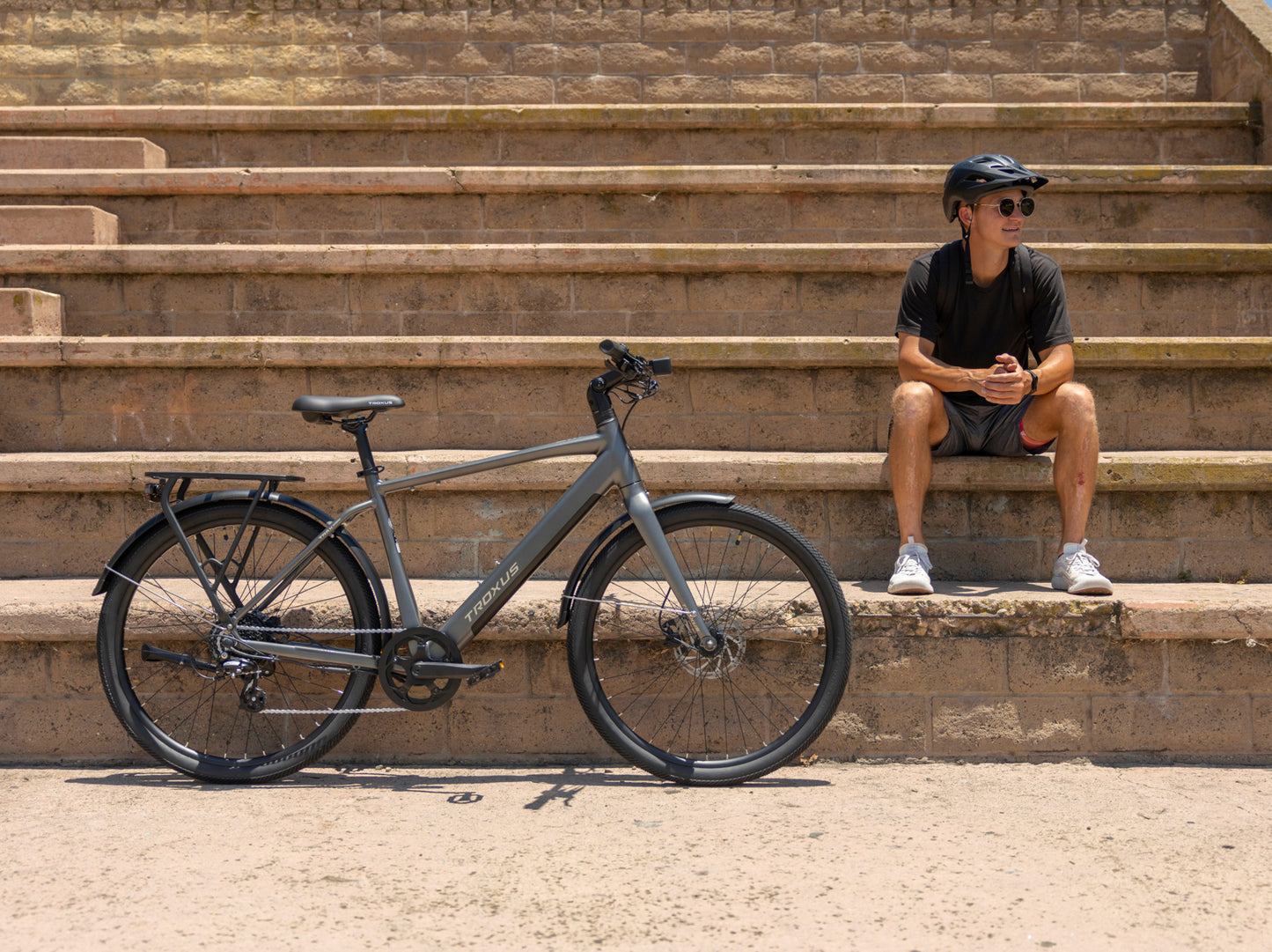 Troxus Trax Sport Natural Slate electric bike parked beside a rider showcasing commuter eBike design and urban mobility